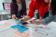 © Tj - Three Asian ux designers are discussing and improving the design of a mobile application during a working meeting, placing different pieces of paper and sticky notes on the table