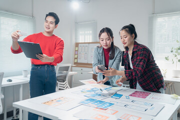 group of young asian ui/ux developer team working and discussing mobile app interface wireframe desi