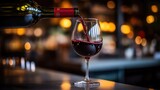 A bottle of red wine is being poured into a glass on a bar counter with a blurred warm bokeh background.
