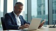 © Nathan - Focused middle-aged Caucasian man using a laptop and tablet in a modern office setting.