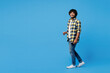 © ViDi Studio - Full body side view young smiling fun happy Indian man he wear yellow checkered shirt casual clothes walk go looking camera isolated on plain blue cyan background studio portrait. Lifestyle concept.
