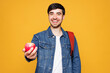 © ViDi Studio - Young smiling happy boy student he wear denim casual clothes backpack bag hold eat give apple fruit stretch hand to camera isolated on plain yellow background. High school university college concept.