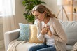 © Akimul - Mature Woman Experiencing Chest Pain at Home Possible Heart Attack or Angina Seeking Relief and Comfort While Sitting on Sofa in Living Room Healthcare and