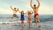 © Lomb - Happy group of young friends jumping on the sea shore at sunset, enjoying summer vacation together. Concept of youth, freedom, travel lifestyle and togetherness for a generation z holiday celebration.