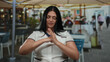 © Krakenimages.com - Young woman with long black hair sitting on an outdoor restaurant terrace, gesturing with her hands, wearing a white uniform, engaging in a casual interaction.