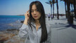 © Krakenimages.com - Woman thinking on a seaside promenade, young woman in striped shirt, palm trees and beach in background, sunny day, asian woman outdoors, thoughtful gesture, casual attire, serene scenery.