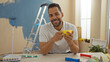 © Krakenimages.com - Young man enjoying coffee indoors amidst home renovation with paint supplies and ladder in background conveying warmth and creativity in new apartment setting