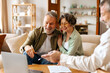 © Home-stock - Senior couple having meeting with designer or broker looking at laptop and discussing choices. Happy older spouses customers choosing flat or house