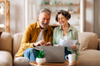 © Home-stock - Happy senior couple with laptop and papers planning family budget together, calculating spends and taxes on retirement, sitting on couch