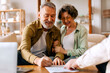 © Home-stock - Happy retired senior couple signing real estate lease contract while meeting with realtor, elderly man and woman filling paper form