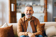 © Home-stock - Portrait of Excited senior man posing alone at home, sitting on couch and smiling, looking at camera in living room