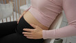 © Krakenimages.com - Pregnant woman sitting indoors with hands on belly in a cozy bedroom near a cradle, symbolizing motherhood and family in a peaceful home environment.