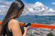 © Daniel Ching - Young Colombian woman using smartphone at scenic overlook in Medellin