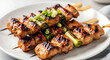 © noz-studio - Close up of chicken skewers with green onions on a white plate ready to be served and enjoyed quickly