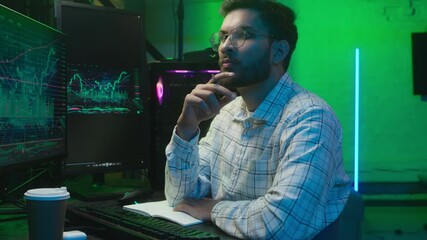 Indian Arabian man businessman programmer hacker IT specialist business male ethnic guy studio home coder trader writing notes code information data looking computer monitor pc worker write analyzing