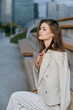 © SHOTPRIME STUDIO - young woman in beige suit sitting on urban bench with thoughtful expression, natural light, casual fashion, city background, autumn mood, professional style