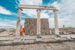 © EdNurg - Tourist with open arms standing between restored and damaged columns of the ancient city of Pergamon, a famous historical site in Turkey