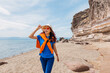 © EdNurg - Young woman enjoying a sunny day at the beach, walking near a beautiful cliff