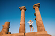 © EdNurg - Cheerful tourist holding her hat while visiting the Temple of Athena in Assos, Turkey, during a sunny day