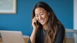 © Phannaporn - A smiling Asian woman engages in a business call, working on a laptop. Capturing a moment of productivity and connection.