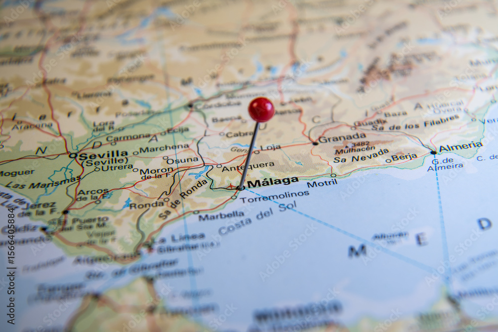 Close-up of a red-headed pin marking the city of Málaga on a world atlas map of Spain, representing travel planning, destination focus, and exploration.