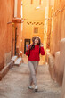 © EdNurg - Young woman tourist with backpack and hat is walking in narrow street of Ait Benhaddou, Morocco, using smartphone app