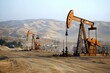 © Nice Seven - Oil pumpjacks operating in a dry, mountainous desert landscape under a clear sky during daytime.