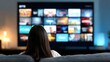© Nice Seven - A person watches a large smart TV screen displaying various streaming options in a dimly lit room.