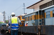 © Poguz.P - Railway Engineer Inspecting Train Cars at a Station, Back View of Worker in Safety Vest at Rail Depot, Industrial Worker Supervising Operations in a Train Yard