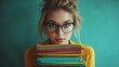 © Thanayut - young woman with glasses holding a colorful stack of files or notebooks in front of teal background