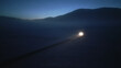 © stockcopter - Nighttime aerial view captures a car's headlights illuminating a winding mountain road, symbolizing the journey ahead and the thrill of alpine driving. Darkness and fog add a sense of mystery.