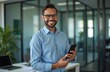 © miss irine - Smiling young Latin business man in office holds phone. Professional executive or employee looks at camera with smartphone. Happy confident businessman at work in modern office. Business concept.