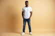 © Vadym - Handsome young Black man poses confidently in casual outfit. He wears white t-shirt blue jeans and sneakers. Serious face expression. Model stands against beige background. Full body shot.