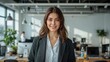 © Diclonius - A confident businesswoman with a warm smile stands in a modern office setting, exuding professionalism and approachability, embodying modern workplace dynamics.