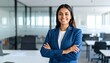 © StocksJust4You - A confident Latin American businesswoman stands smiling in a modern office - radiating professionalism, success, and readiness in a contemporary corporate environment