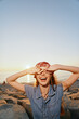 © SHOTPRIME STUDIO - Lifestyle woman wearing modern boho-western denim street style laughing joyfully at sunset by the rocky shore with warm film color tones creating a relaxed vibe.