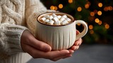 Cozy scene of hands holding a steaming mug of hot chocolate topped with marshmallows against a blurred festive background of bokeh lights