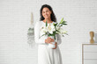 © Pixel-Shot - Beautiful young happy African-American woman holding vase with bouquet of white lily flowers near brick wall at home