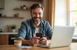 © Pete - Smiling mid-adult man uses mobile phone, laptop at home dining table. Holds credit card, suggesting online shopping financial transactions. Casual domestic scene shows happy lifestyle with technology.