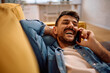 © Drazen - Happy man making phone call while relaxing on couch at home.
