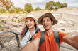 © EdNurg - Smiling couple capturing a joyful selfie amidst ancient ruins at an archaeological site, enjoying their travel adventure