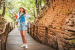 © EdNurg - Female tourist holding smartphone navigating and exploring ancient ruins walking on wooden walkway