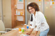 © WavebreakMediaMicro - African American woman leaning over desk reviewing swatches with brush and paint jars in studio