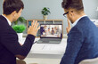 © Studio Romantic - Video meeting. Two businessmen talking on web conference with group of colleagues using laptop web camera. Back view of two men waving welcoming colleagues to online business meeting.