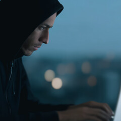 Wall Mural - midnight code: a hooded individual engrossed in coding on a laptop, set against a darkened, urban ba