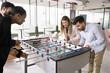 © fizkes - Casual office fun. Joyful enthusiastic multiethnic workmates colleagues engaged in friendly competition play foosball match divided into teams enjoy funny teambuilding activity playful spirit unity