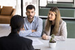 © fizkes - Seeking advice. Attentive family couple clients of bank manager real estate agent broker discuss terms conditions of loan mortgage agreement life insurance policy investment options of buying business