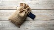 © FARIHA - Burlap gift bag with a dark blue tag rests on a wooden surface
