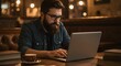 © ForAll - Man with beard and glasses working on a laptop in a cafe with coffee and books on the table near him