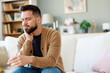 © Dorde - Young Man in Beige Cardigan Expressing Discomfort in Well-Lit Living Room with Neutral Decor